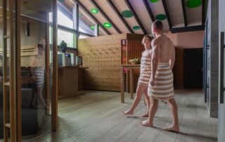 Paar in Badebekleidung im Wellnessbereich des Hotels Alpenglück, umgeben von Holz und sanfter Beleuchtung beim Familienurlaub.