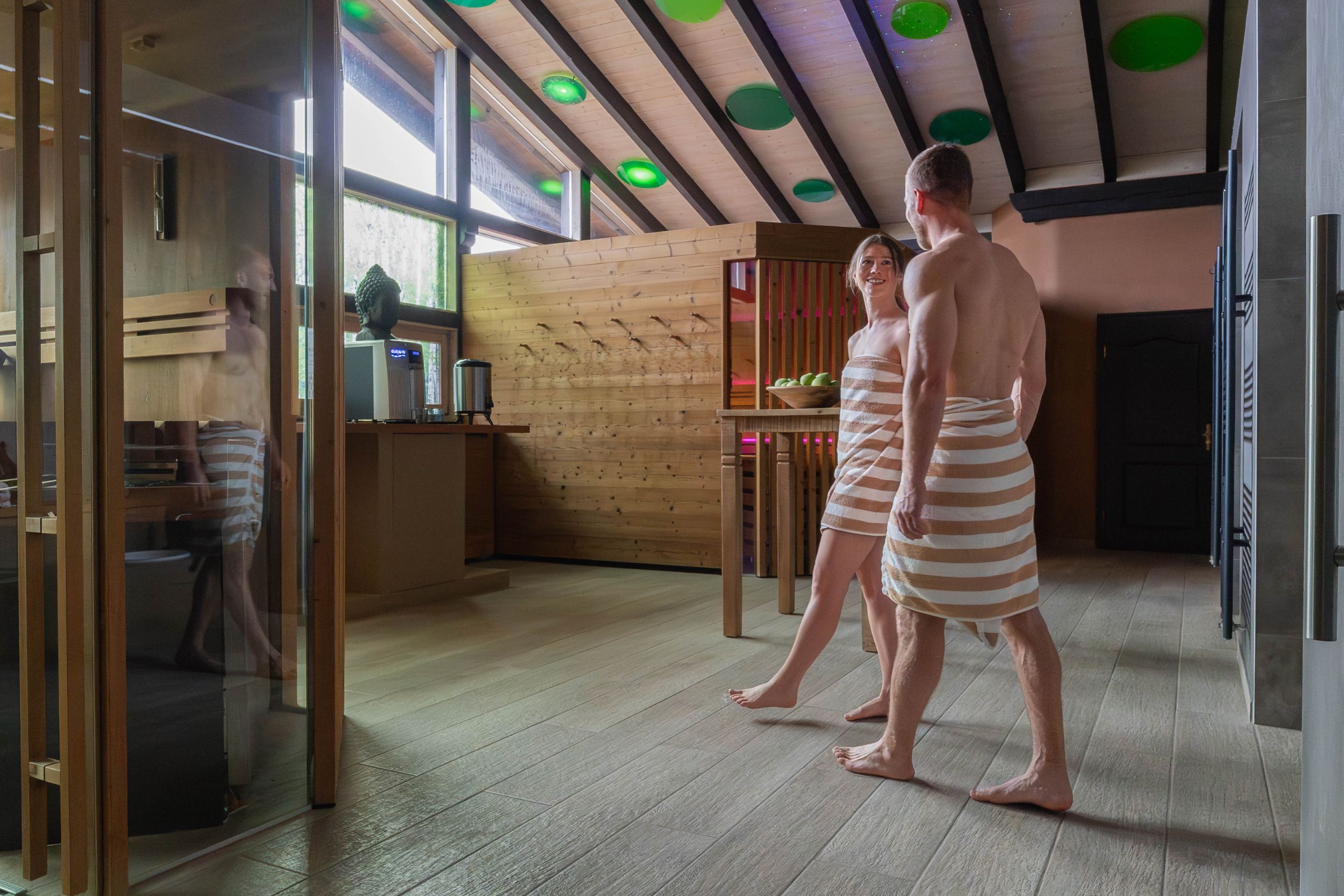 Paar in Badebekleidung im Wellnessbereich des Hotels Alpenglück, umgeben von Holz und sanfter Beleuchtung beim Familienurlaub.