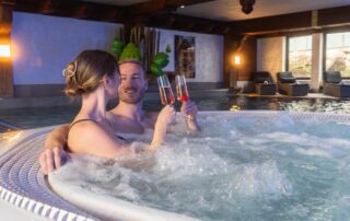Ein Paar entspannt im Whirlpool eines Wellnesshotels, genießt Sekt und eine romantische Auszeit bei entspannenden Wasserblasen.