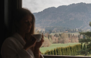 Frau mit einer Tasse in einem Hotelzimmer mit Blick auf die Berge und die malerische Natur im Familienurlaub.
