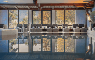 Wellnessbereich des Hotels mit Indoor-Pool und Liegen, umgeben von großen Fenstern und herbstlicher Natur im Hintergrund.