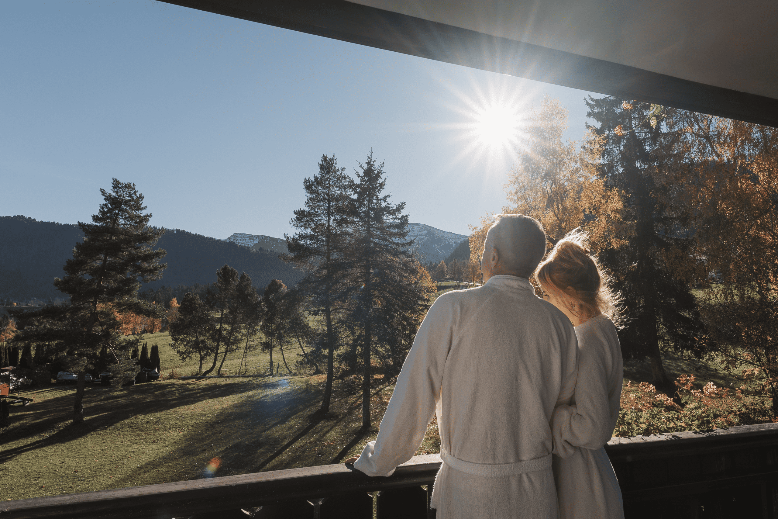 Paar im Bademantel genießt den Ausblick auf die Berge und Wälder vom Balkon eines Hotels in der Natur.